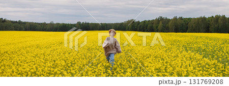 Banner smiling 9 year old girl in oversize sweater running in yellow rapeseed field 131769208