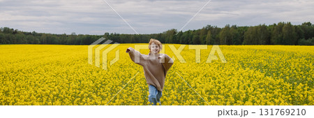 Banner smiling 9 year old girl in oversize sweater running in yellow rapeseed field 131769210