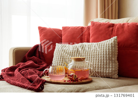 Glass Teapot and Teacup with Pomegranate Drink with Ginger and Citrus on Cozy Sofa with Autumn Decor Glass Teapot and Teacup with Pomegranate Drink with Ginger and Citrus on Cozy Sofa with Autumn Decor 131769401