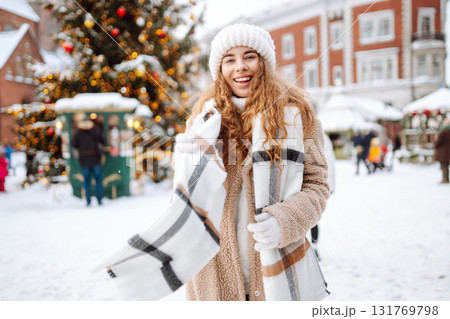 Young happy woman in a winter coat and scarf walks along a snowy city street. Concept of style. Young happy woman in a winter coat and scarf walks along a snowy city street. Concept of style. 131769798