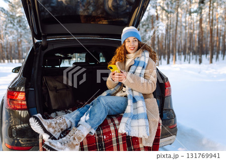 Happy Woman sitting in trunk, using phone. Snowy weather. Concept of adventure, travel by car. Happy Woman sitting in trunk, using phone. Snowy weather. Concept of adventure, travel by car. 131769941