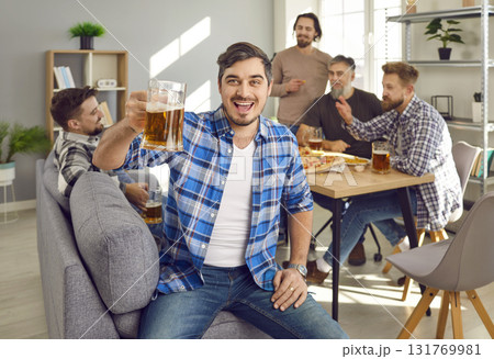 Portrait of man holding glass of beer with a company of friends talking in the background. Portrait of man holding glass of beer with a company of friends talking in the background. 131769981