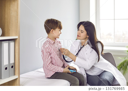 Doctor with stethoscope examining child's lungs and heart rate sitting on the couch in office. Doctor with stethoscope examining child's lungs and heart rate sitting on the couch in office. 131769985