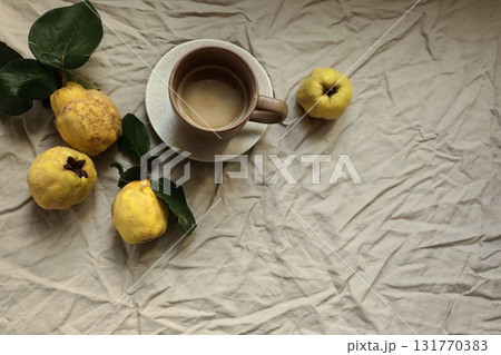 Rustic fall still life with fresh yellow quinces, cup of hot drink, coffee on crumpled linen fabric background. Cozy autumn mood, natural light. Seasonal fruit harvest concept. Flat lay, top view Rustic fall still life with fresh yellow quinces, cup of hot drink, coffee on crumpled linen fabric background. Cozy autumn mood, natural light. Seasonal fruit harvest concept. Flat lay, top view 131770383
