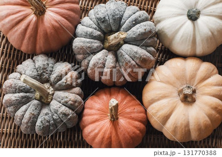 Closeup of assorted pumpkins in soft earthy tones arranged on rustic wicker surface background. Autumn harvest still life. Organic seasonal vegetables. Fall decor, Thanksgiving cozy seasonal mood. Closeup of assorted pumpkins in soft earthy tones arranged on rustic wicker surface background. Autumn harvest still life. Organic seasonal vegetables. Fall decor, Thanksgiving cozy seasonal mood. 131770388