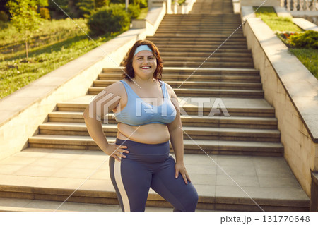 Fat woman wearing sportswear standing in park drinking a water after fit exercises outdoors. Fat woman wearing sportswear standing in park drinking a water after fit exercises outdoors. 131770648