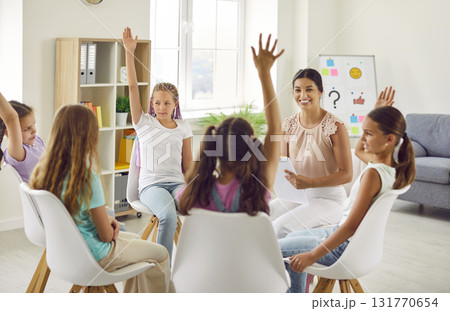 Group of school children girls sitting in a circle with psychologist and raising hands up. Group of school children girls sitting in a circle with psychologist and raising hands up. 131770654
