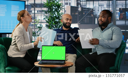 Business people negotiate to align on vision next to mockup display on laptop, using data driven insights and cultural diversity to support leadership and corporate success. Camera B. 131771057