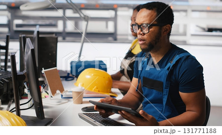Engineer investigating malfunctioning systems in photovoltaics factory, comparing parameters with pc and tablet. Black man inspecting solar panels manufacturing plant, high tech. Camera A. Engineer investigating malfunctioning systems in photovoltaics factory, comparing parameters with pc and tablet. Black man inspecting solar panels manufacturing plant, high tech. Camera A. 131771188