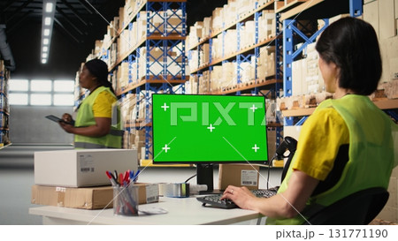 Logistics worker manages orders next to green screen display, showcasing warehouse automation tools and inventory control dashboards. E-commerce order processing with storage racks. Camera A. 131771190