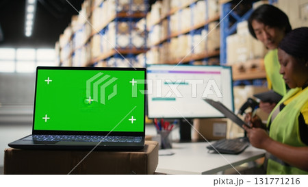 Warehouse staff works next to green screen on computer display, managing shipping labels and order fulfillment or e-commerce inventory systems in industrial storage room. Camera A. Warehouse staff works next to green screen on computer display, managing shipping labels and order fulfillment or e-commerce inventory systems in industrial storage room. Camera A. 131771216