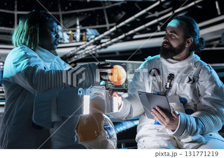 Team of astronauts in starship travelling to Mars conducting safety checks using tablet. Teamworking cosmonauts flying to red planet operating spacecraft control interface, calibrating sensors 131771219