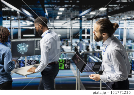 Worried technician in server room detecting hacking attempt targeting data systems and panicking about data breach. Engineering team under pressure by virus activity, emergency protocol. 131771230