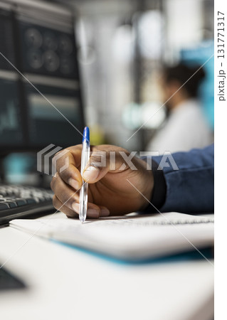 Close up of black business analyst takes notes on textbook in the office, examining charts and graphs to align company objectives with strategy. Drive progress and measurable performance. 131771317
