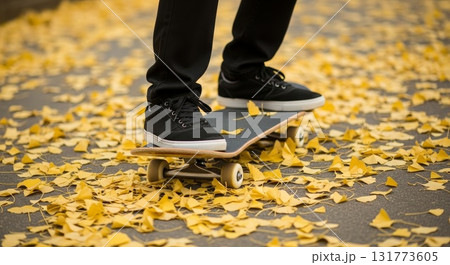 Person skateboarding on asphalt pavement covered with golden yellow autumn leaves wearing black canvas sneakers and dark pants 131773605