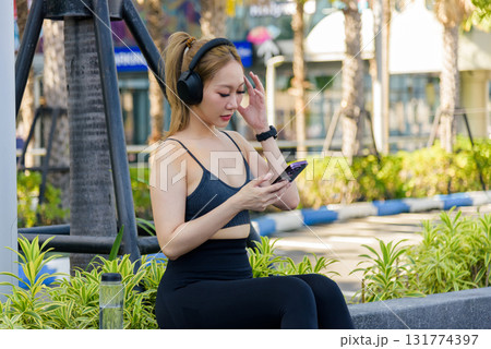 Sport woman enjoys active outdoor exercise workout stretch, fit people pause for break while asian female checking phone with headphones, healthy sport activity continues. 131774397