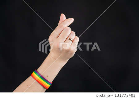 Woman with wedding ring and rainbow bracelet showing heart sign on black background.  131775403