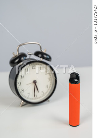 Disposable vape and alarm clock on white background. Disposable vape and alarm clock on white background. 131775427