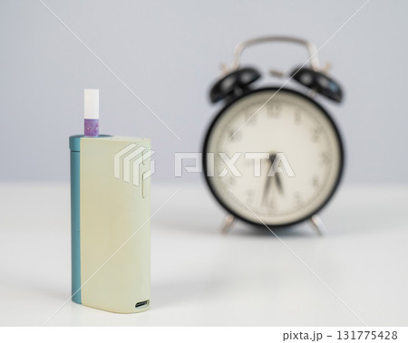 Electronic cigarette and alarm clock on white background. Tobacco heating systems. Electronic cigarette and alarm clock on white background. Tobacco heating systems. 131775428