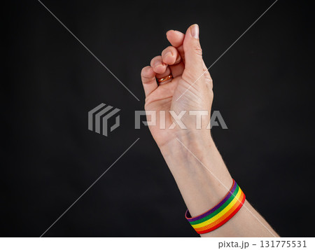 Woman with wedding ring and rainbow bracelet showing heart sign on black background.  131775531