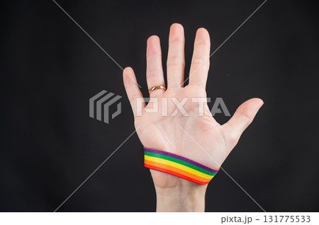 Woman with wedding ring and rainbow bracelet holding palm on black background.  131775533