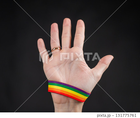 Woman with wedding ring and rainbow bracelet holding palm on black background.  131775761