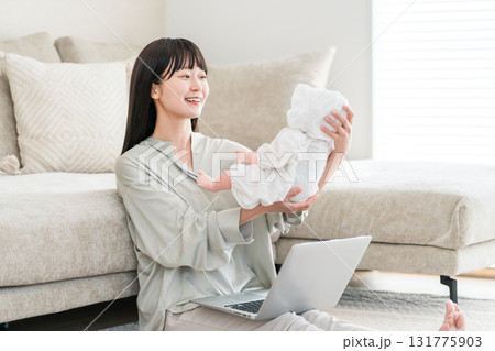 赤ん坊を抱っこしながらパソコンを見る若いアジア人女性 131775903