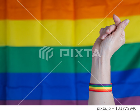 Woman wearing rainbow flag bracelet making heart gesture with fingers.  131775940
