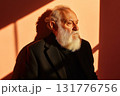 Elderly man with thick white beard stands alone on beige background under soft sunlight 131776756