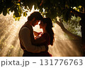 Young couple embraces under sunlight filtering through a large tree in a romantic moment 131776763