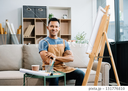 Asian male painter do artwork in art workshop, painting supplies, oil pastels, two canvas easel, creative space with paintbrush in art studio 131776810