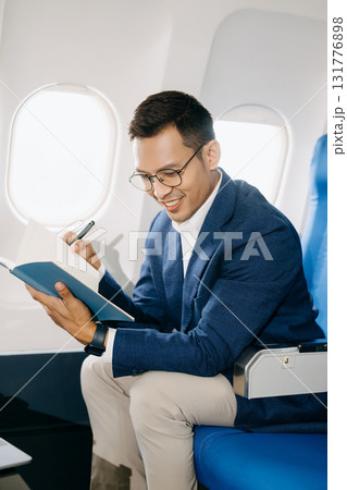 Attractive Asian male passenger of airplane sitting in comfortable seat while working laptop and tablet with mock up area using wireless connection. Attractive Asian male passenger of airplane sitting in comfortable seat while working laptop and tablet with mock up area using wireless connection. 131776898
