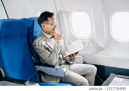 Attractive Asian male passenger of airplane sitting in comfortable seat while working laptop and tablet with mock up area using wireless connection. 131776900
