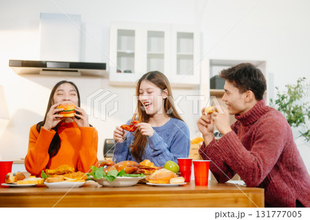 Young Asian friends enjoy a cozy dinner party at home, sharing food, drinks, and laughter in a warm modern kitchen. 131777005