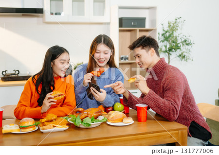 Young Asian friends enjoy a cozy dinner party at home, sharing food, drinks, and laughter in a warm modern kitchen. 131777006