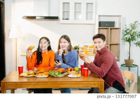 Young Asian friends enjoy a cozy dinner party at home, sharing food, drinks, and laughter in a warm modern kitchen. 131777007