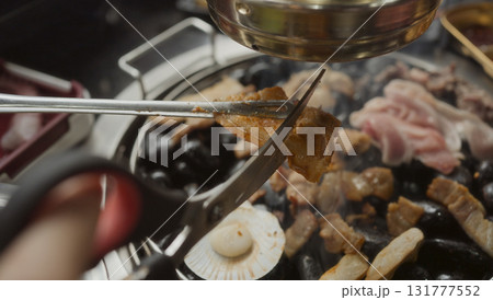 Hand cooking smoked grilled pork on iron grill pan in Korean BBQ in restaurant. Traditional Korea style food barbecue pork belly steak on charcoal grill. 131777552