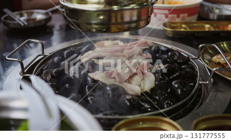 Hand cooking smoked grilled pork on iron grill pan in Korean BBQ in restaurant. Traditional Korea style food barbecue pork belly steak on charcoal grill. 131777555