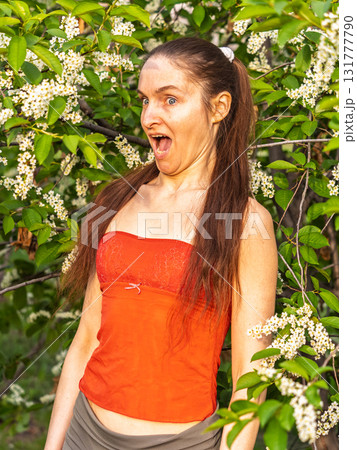 Young woman sneezes in the park against the background of a flowering tree. Allergy to pollen concept. Young woman sneezes in the park against the background of a flowering tree. Allergy to pollen concept. 131777790