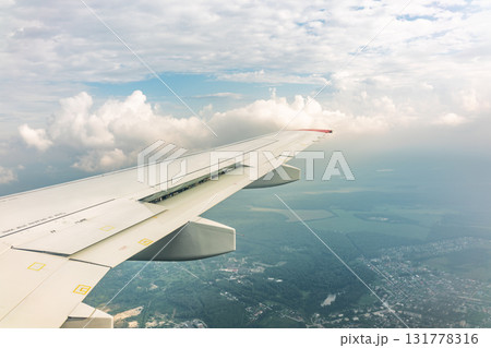 View of airplane wing, blue skies and green land during landing. Airplane window view. 131778316