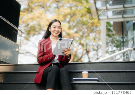 Confident Asian woman with a smile standing holding notepad and tablet at out side office. Confident Asian woman with a smile standing holding notepad and tablet at out side office. 131778463