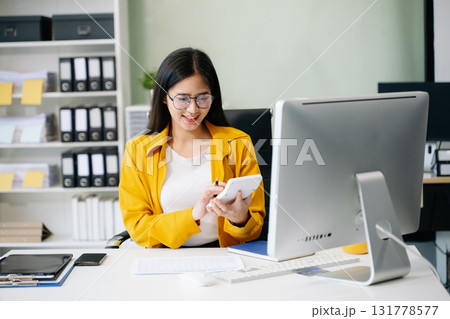 Young Asian businesswoman working with working notepad, tablet and laptop documents talking 131778577