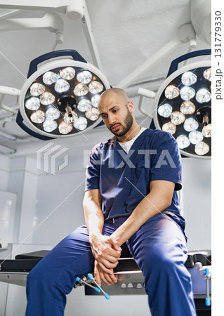 A surgeon takes a moment to rest in an operating room, illuminated by surgical lights. 131779330