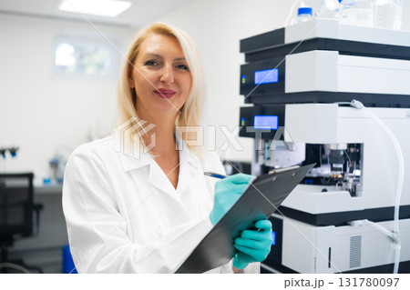Experienced woman researcher recording chromatography results during HPLC analysis in a modern lab. Concept of chemical testing and innovation. 131780097