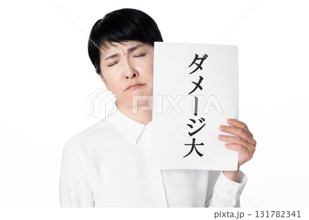 ダメージ大と書かれた紙を片手で持ち眉間にシワを寄せ目をつぶるシニア女性 131782341