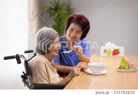 Caregiver feeding elderly asian woman with soup. Caregiver feeding elderly asian woman with soup. 131782630