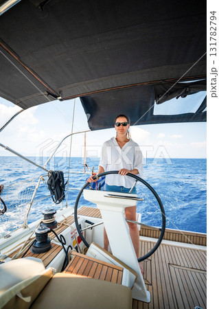 Young woman steering a sailing yacht near Croatia, confidently standing at the helm. Female leadership, empowerment and freedom in maritime lifestyle. 131782794