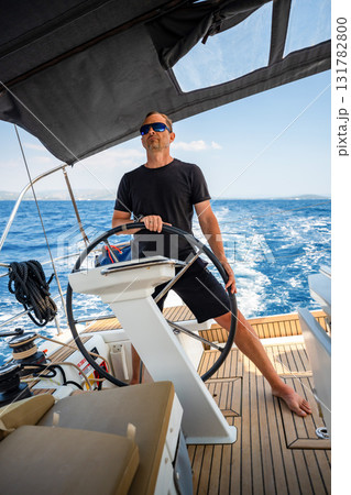 Man standing at the helm of a sailing yacht near Croatia, steering the boat through open water. Leadership, control, sailing lifestyle and freedom at sea. 131782800