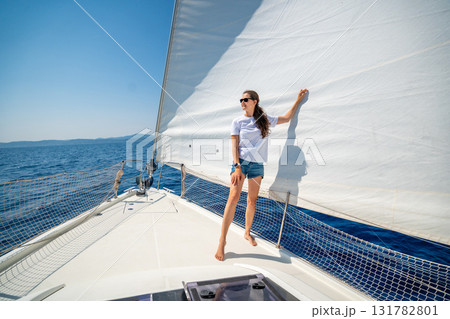 Young woman standing on the bow of a sailing yacht during a sea journey. Freedom, wind, and mindful solitude in maritime travel 131782801