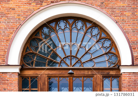A grand arched window with decorative wooden frame. Front view, background photo 131786031